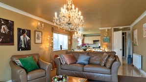 A living room with a chandelier, a sofa, a coffee table with a bowl, and artwork on the walls. - Apartment in Newquay Near Stunning Beaches (Newquay)