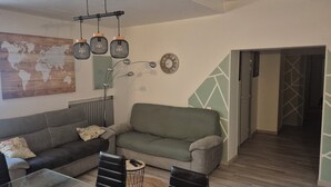 Un salon avec deux canapés, une table basse et un téléviseur. Il y a une carte du monde accrochée au mur et une horloge.