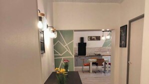 Un couloir mène à une salle à manger dotée d’un plancher en bois, d’une petite table avec des chaises et d’un vase rempli de fleurs, posé sur un comptoir.