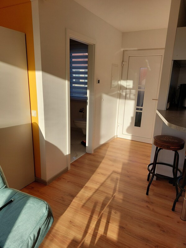 A room with wooden flooring, a kitchenette, a door leading to a balcony, and a small stool. - Small but nice, for relaxing. WWW like forest, water, meadow. (Grünheide (Mark))