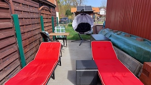 A patio area with two red lounge chairs, a table, and a hanging chair. - Small but nice, for relaxing. WWW like forest, water, meadow. (Grünheide (Mark))