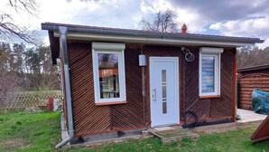 A small, single-story building with a white door and two windows, surrounded by a grassy yard and a wooden fence. - Small but nice, for relaxing. WWW like forest, water, meadow. (Grünheide (Mark))