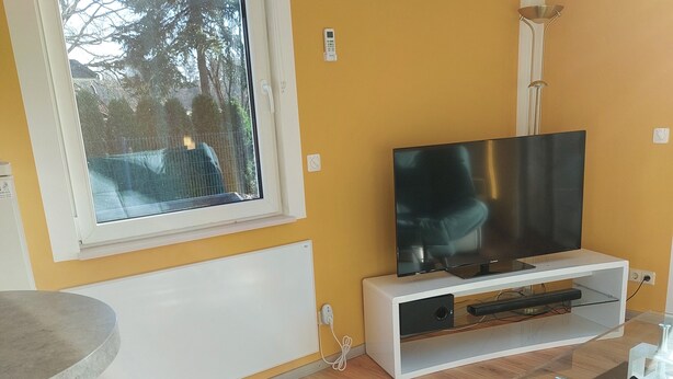 A modern living room with a large window, a flat-screen TV, and a white entertainment unit. - Small but nice, for relaxing. WWW like forest, water, meadow. (Grünheide (Mark))