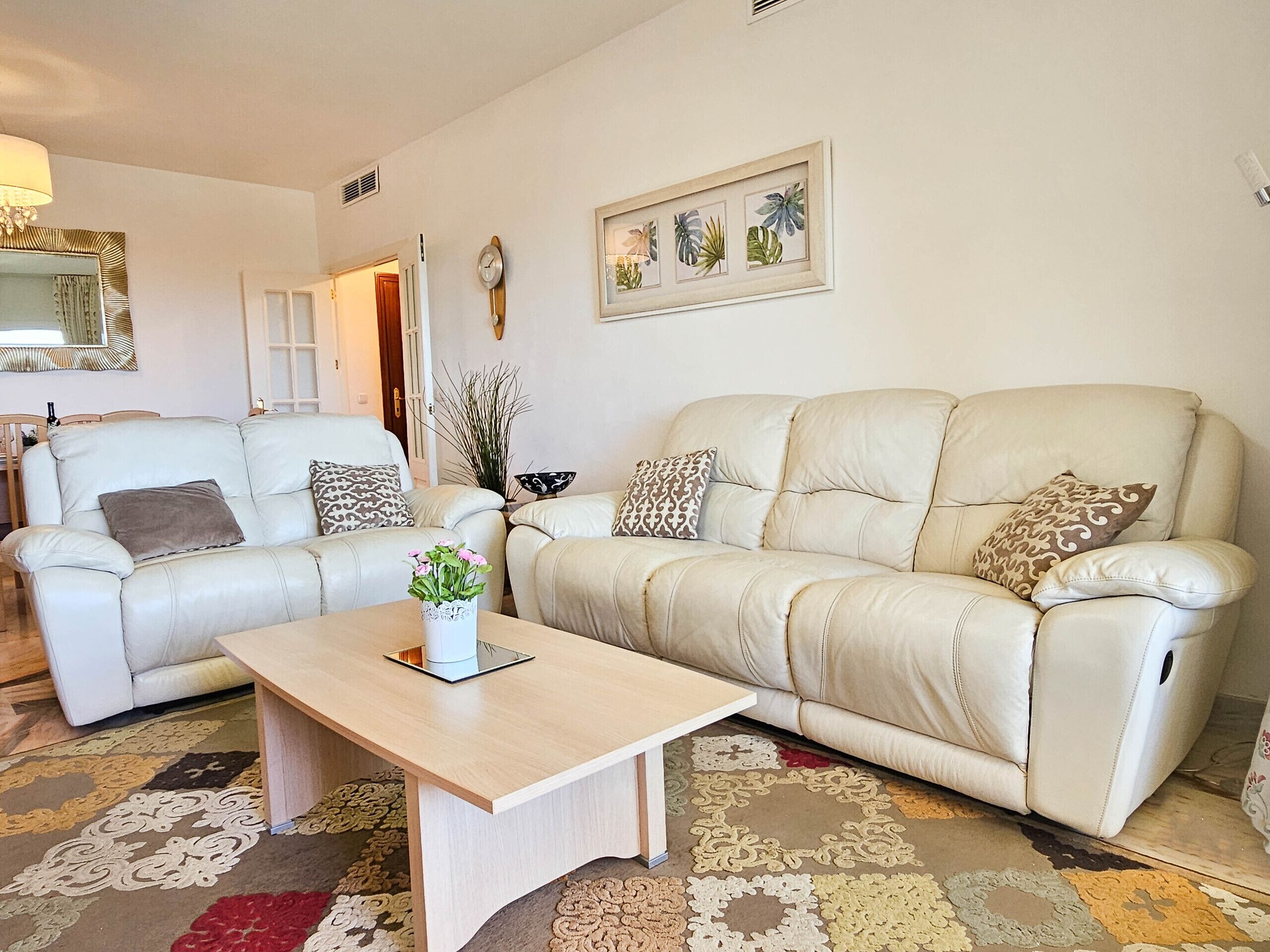 Ein Wohnzimmer mit zwei weißen Ledersofas, einem Holztisch und einem gemusterten Teppich.
