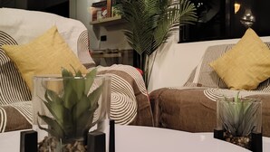 A modern living room with two sofas, each with striped cushions and a yellow pillow. There are two glass vases with plants on a white table.