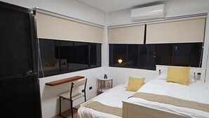 A hotel room with two beds, a desk, a chair, a small table, and a window.