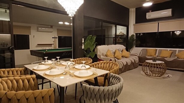 A modern living room with a dining area, a chandelier, and a pool table.
