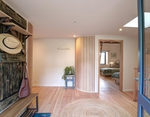 A hallway with wooden flooring, a bench, a wall-mounted hat rack, a small table with a plant, and a bed in the background.