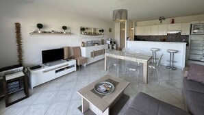 A modern living room with a TV, sofa, coffee table, and a dining area with chairs and a bar. - Apartment with large terrace and garage in Cavalaire-sur-Mer (Cavalaire-sur-Mer)