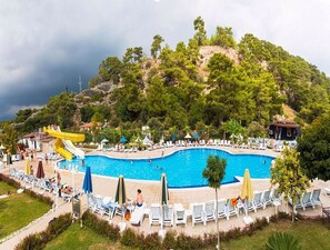 A pool area with a water slide, lounge chairs, and a view of a hilly landscape. - Mir'amor Hotel & Spa - All inclusive (Kemer)