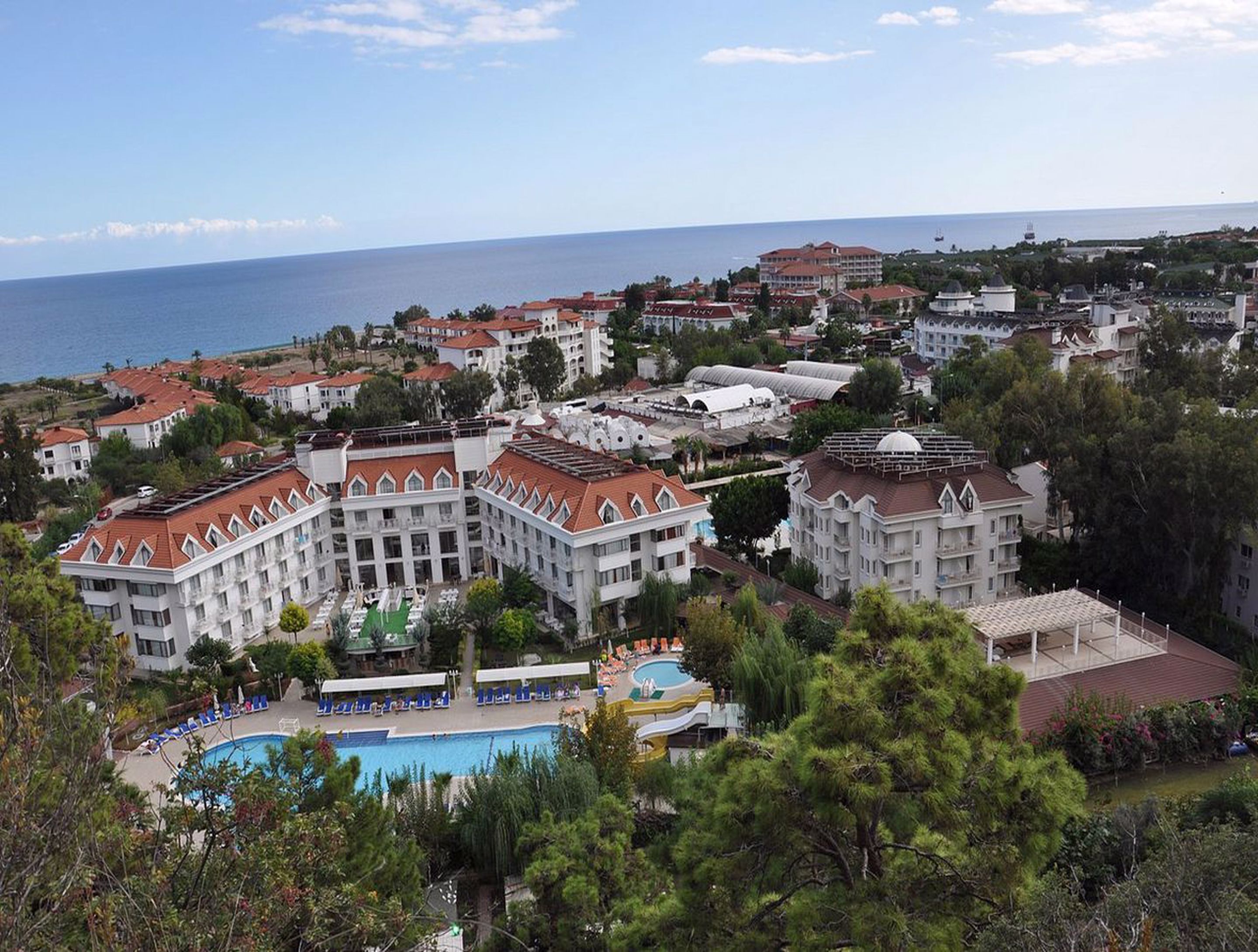 Un resort con varias edificaciones, una piscina y vista al mar.