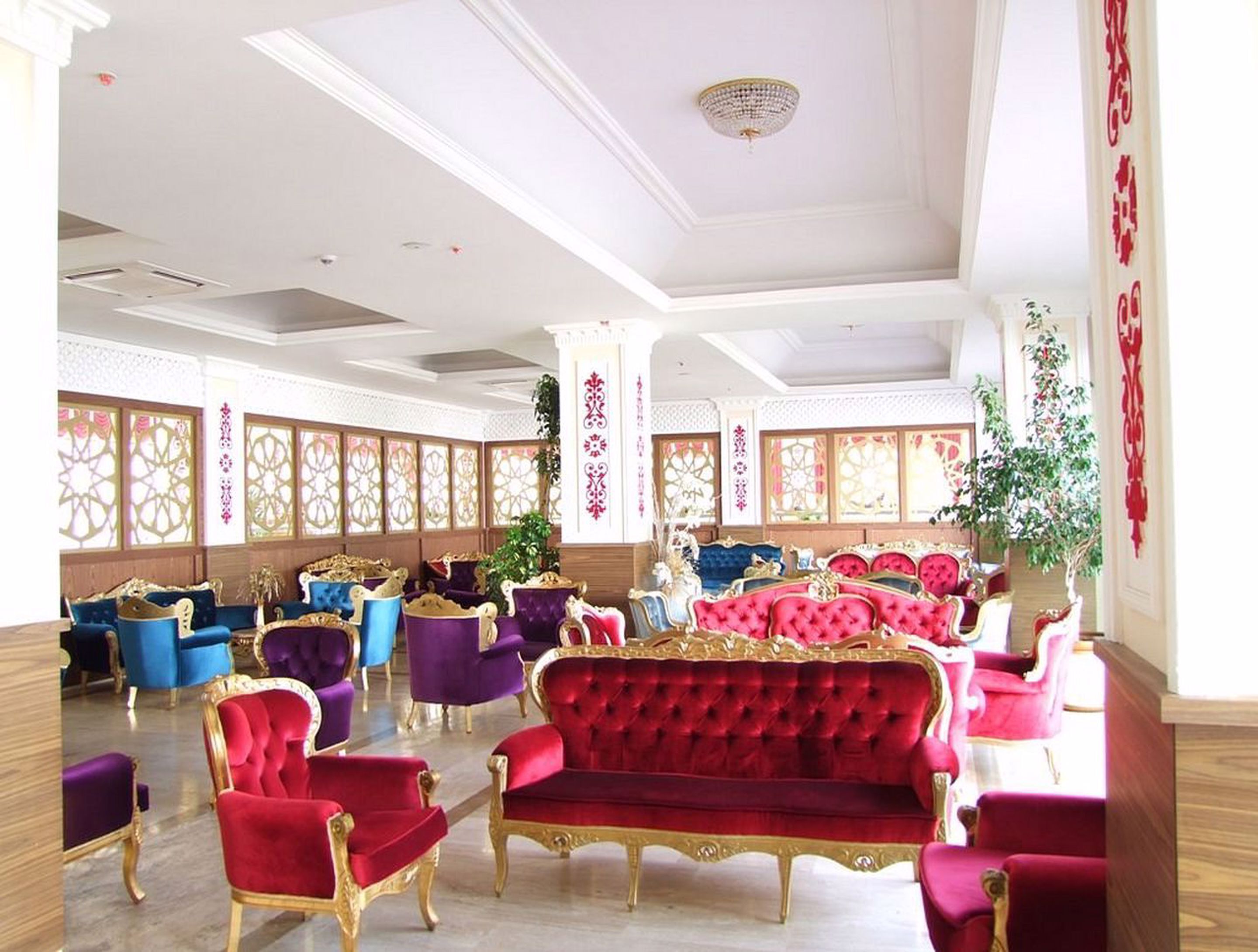 A spacious room with multiple seating options including red and blue upholstered chairs and sofas, a chandelier, and decorative wall panels.