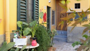 Un edificio amarillo con puerta de madera, un hidrante rojo y macetas con plantas.