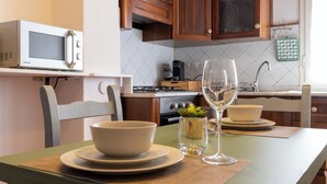 Una cocina con armarios de madera, microondas, cafetera y una mesa de comedor preparada con cuencos y copas de vino.