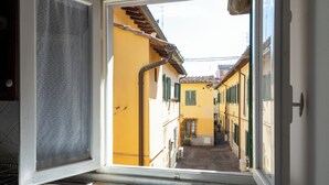 Un estrecho callejón con edificios amarillos y contraventanas verdes, visto desde una ventana donde se ve un lavamanos de metal.