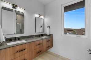Une salle de bain moderne avec un grand miroir, deux lavabos et une fenêtre donnant sur l’extérieur.