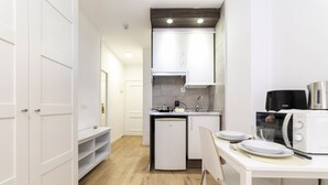 Cocina compacta con muebles blancos, un refrigerador pequeño, microondas y un comedor con mesa y sillas.