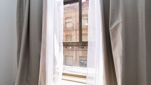 Una ventana con cortinas de gasa, vista de un edificio de ladrillo y un alfeizar visible.