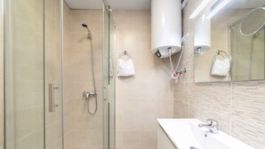Un baño moderno con ducha envuelta en vidrio, un lavamanos blanco y un espejo con una toalla colgada en la pared.