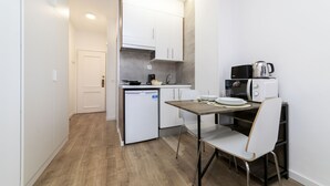 Una cocina compacta con armarios blancos, un refrigerador pequeño, un microondas y una cafetera.