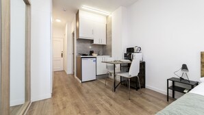 Cocina compacta con armarios blancos, lavavajillas y cafetera. Hay una pequeña mesa de comedor con una silla.