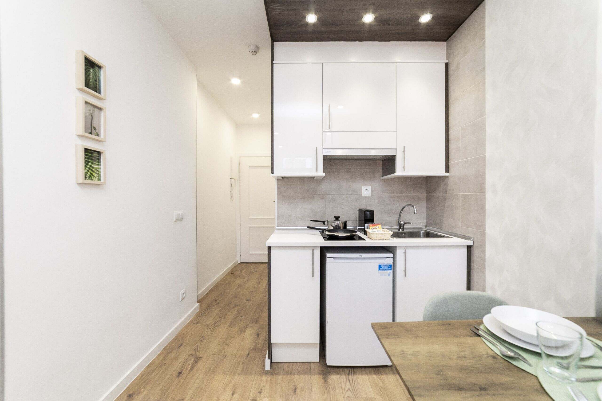 A compact kitchen with white cabinetry, a built-in dishwasher, and a small dining area with a wooden table and chairs.