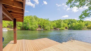 A wooden deck extending over a body of water, surrounded by lush green trees and a clear sky. - Private lakefront home with dock, forest views, balconies, game room, and cozy indoor charm (Dublin)