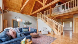 A spacious living room with a blue sofa, a wooden staircase, and a mounted deer head. - Private lakefront home with dock, forest views, balconies, game room, and cozy indoor charm (Dublin)