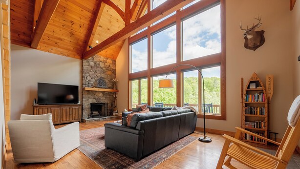 A spacious living room with a large black sectional sofa, a stone fireplace, a television, and a bookshelf. - Private lakefront home with dock, forest views, balconies, game room, and cozy indoor charm (Dublin)