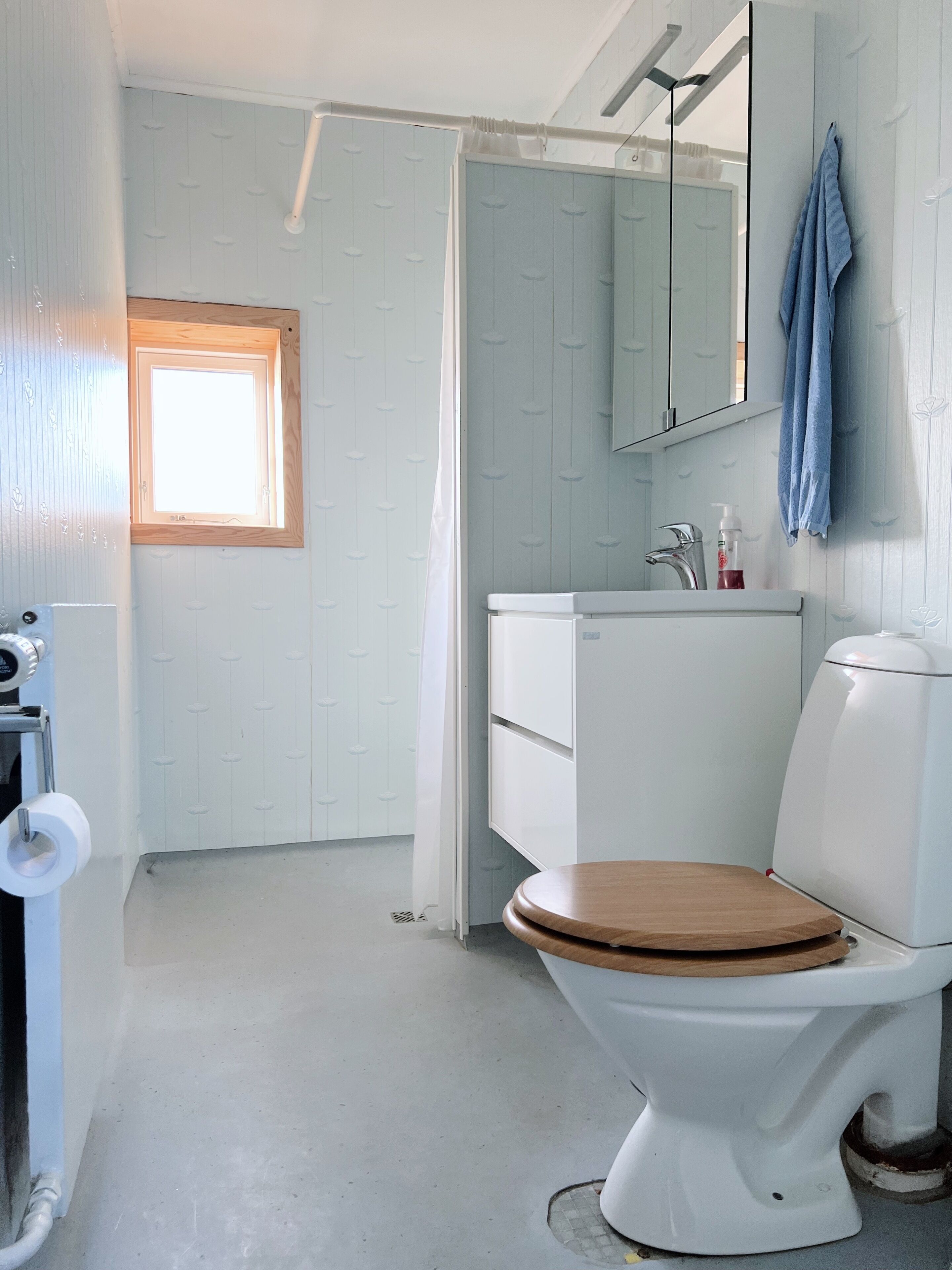A bathroom with a white toilet, a wooden seat, a white sink, and a mirror above it.