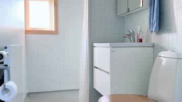 A bathroom with a white toilet, a wooden seat, a white sink, and a mirror above it.