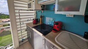 Cocina compacta con microondas, tostadora y cafetera sobre la encimera, un lavabo y una ventana con vistas a un paisaje verde.