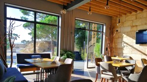 Un espace repas moderne doté de grandes fenêtres, de poutres en bois au plafond et d’une variété de sièges, notamment des tables et des chaises.