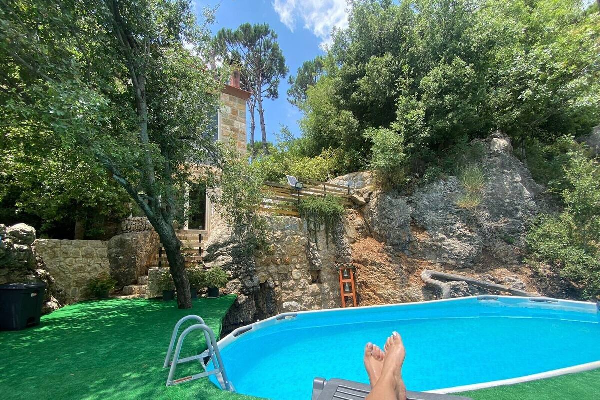 A swimming pool with a ladder, surrounded by green artificial grass and trees.