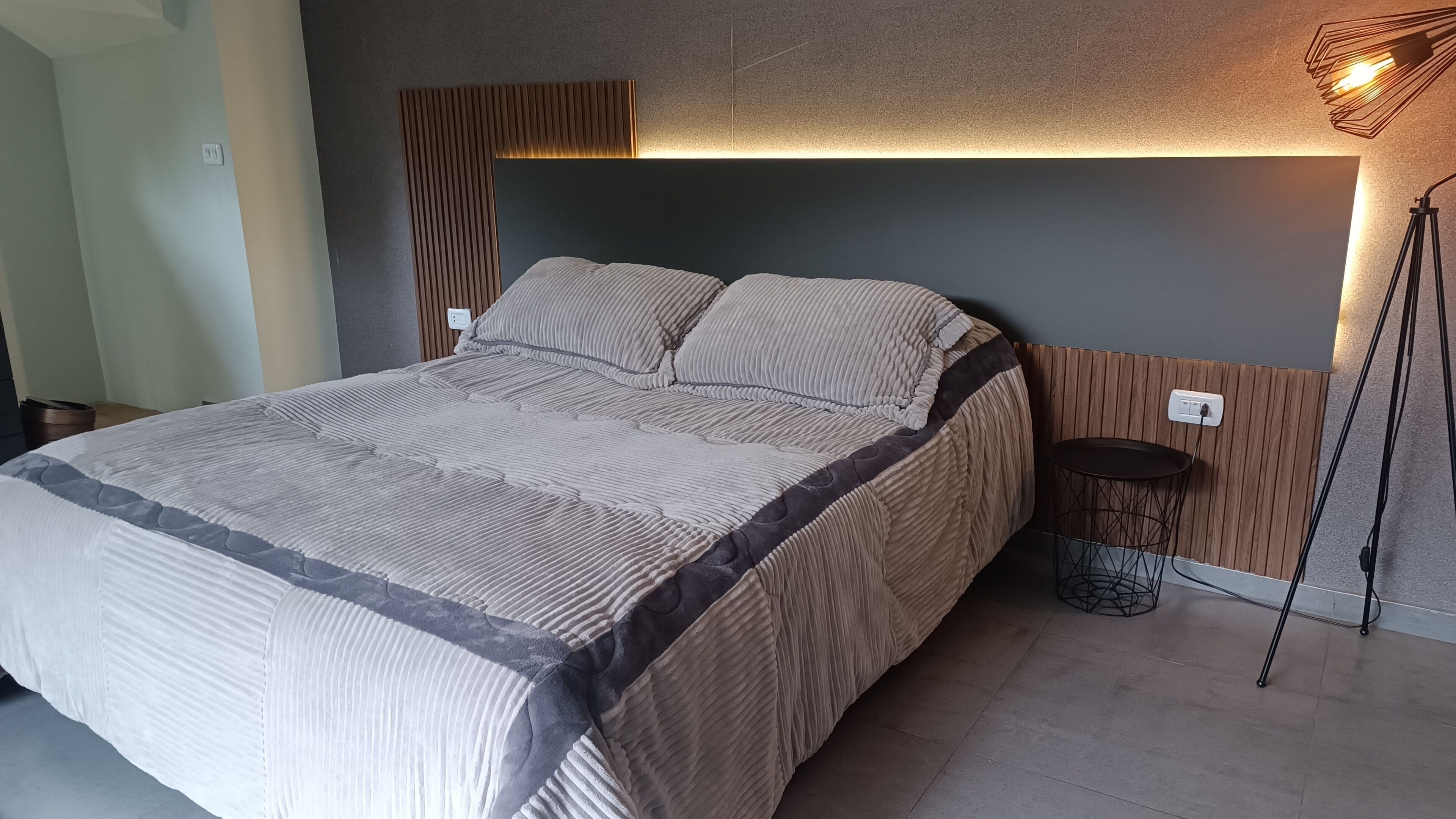 A modern bedroom with a large bed, a wooden headboard, and a bedside table with a lamp.