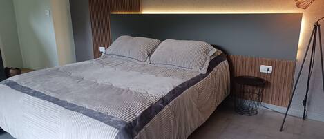 A modern bedroom with a large bed, a wooden headboard, and a bedside table with a lamp.