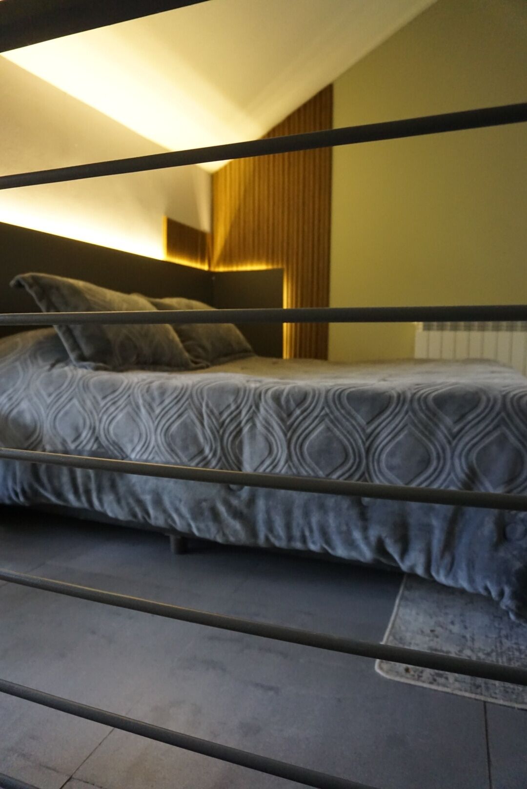 A bunk bed with a patterned bedspread, a headboard with vertical slats, and a radiator on the wall.