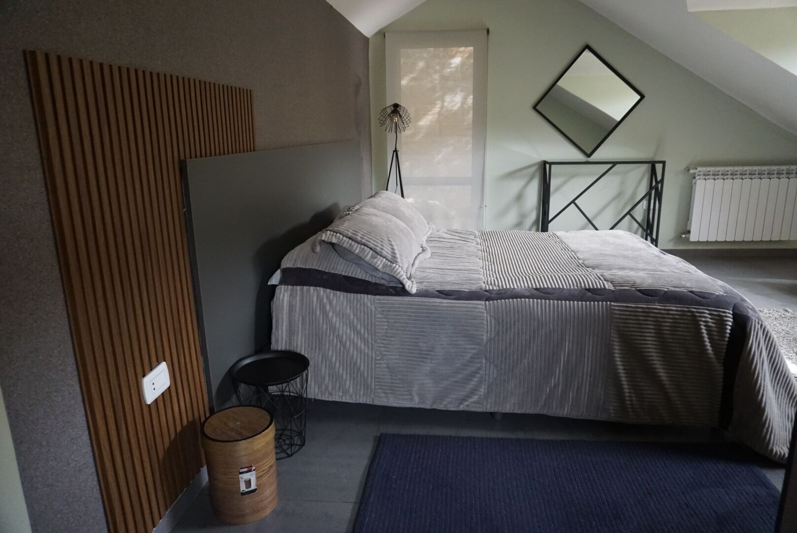 A bedroom with a bed, a standing lamp, a radiator, and a small round table.