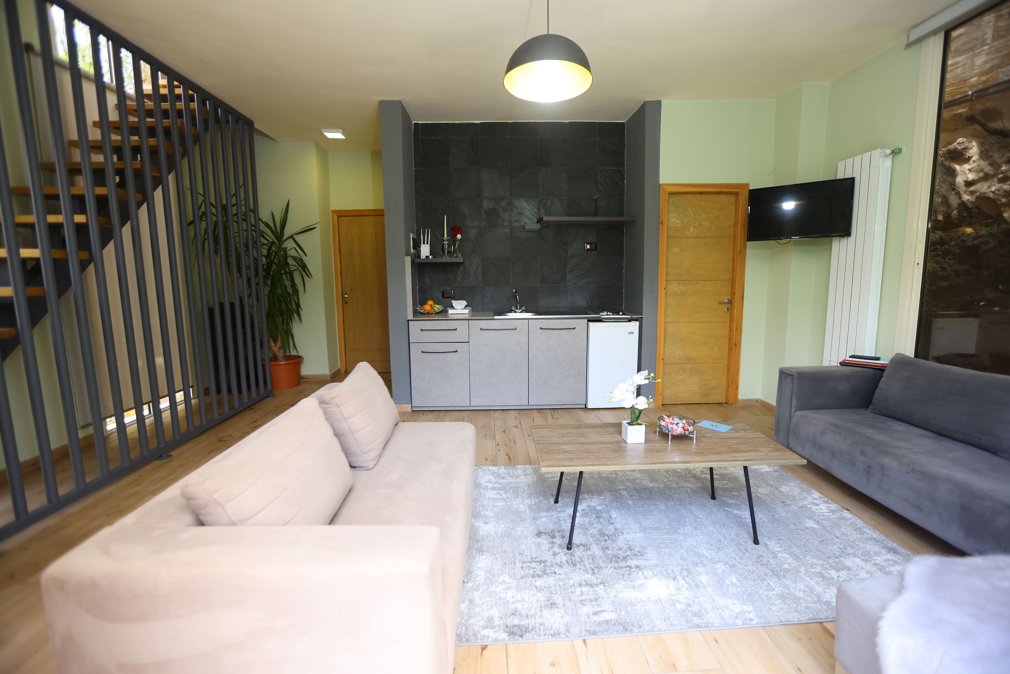 Una sala de estar moderna con un sofá gris, un sofá color beige, un tapete gris y una escalera con barandilla negra.