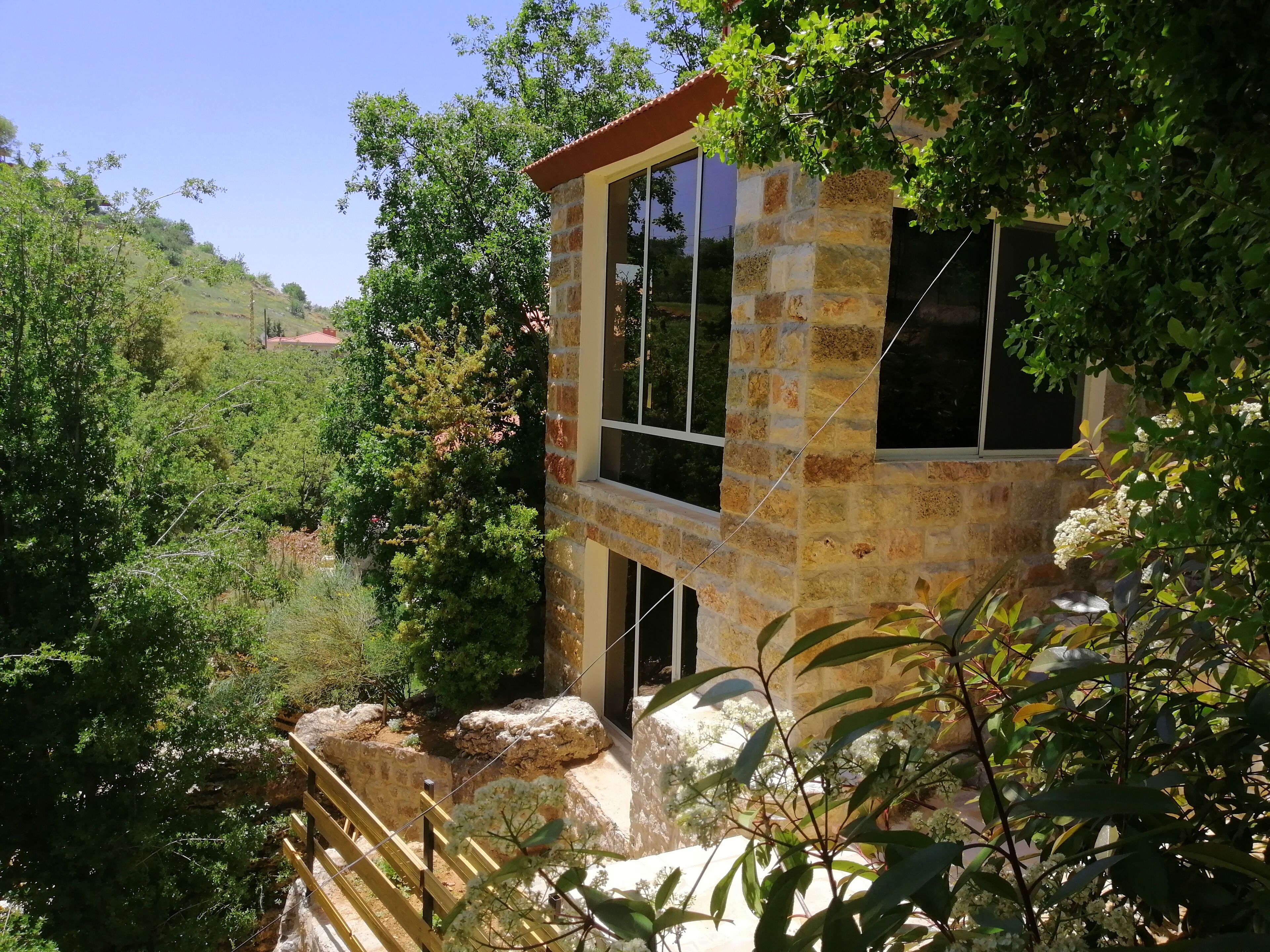 A stone building with large windows, surrounded by lush greenery and trees.
