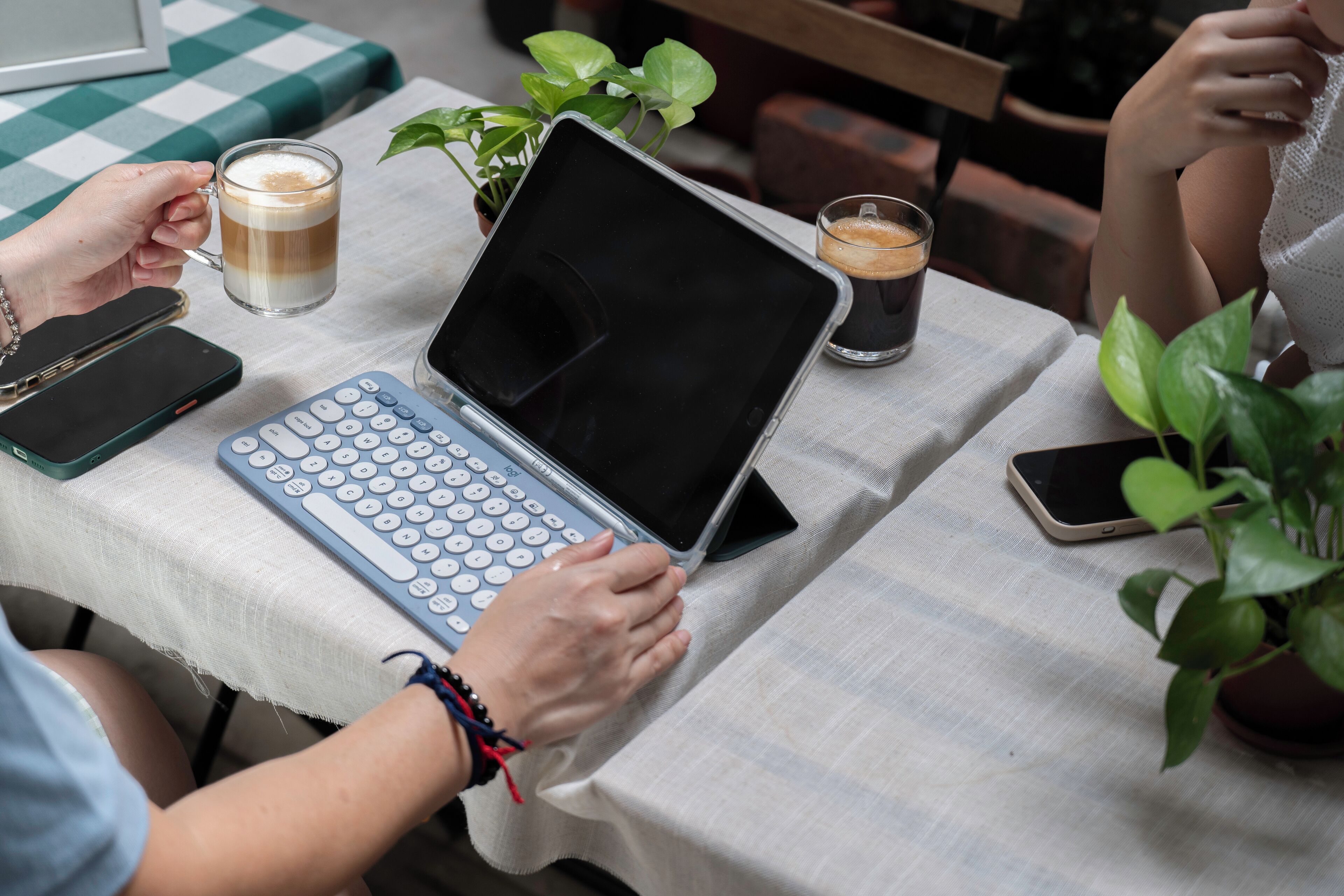 Iemand gebruikt een laptop op een tafel, samen met een toetsenbord, een smartphone, een tablet en twee koffiekopjes.