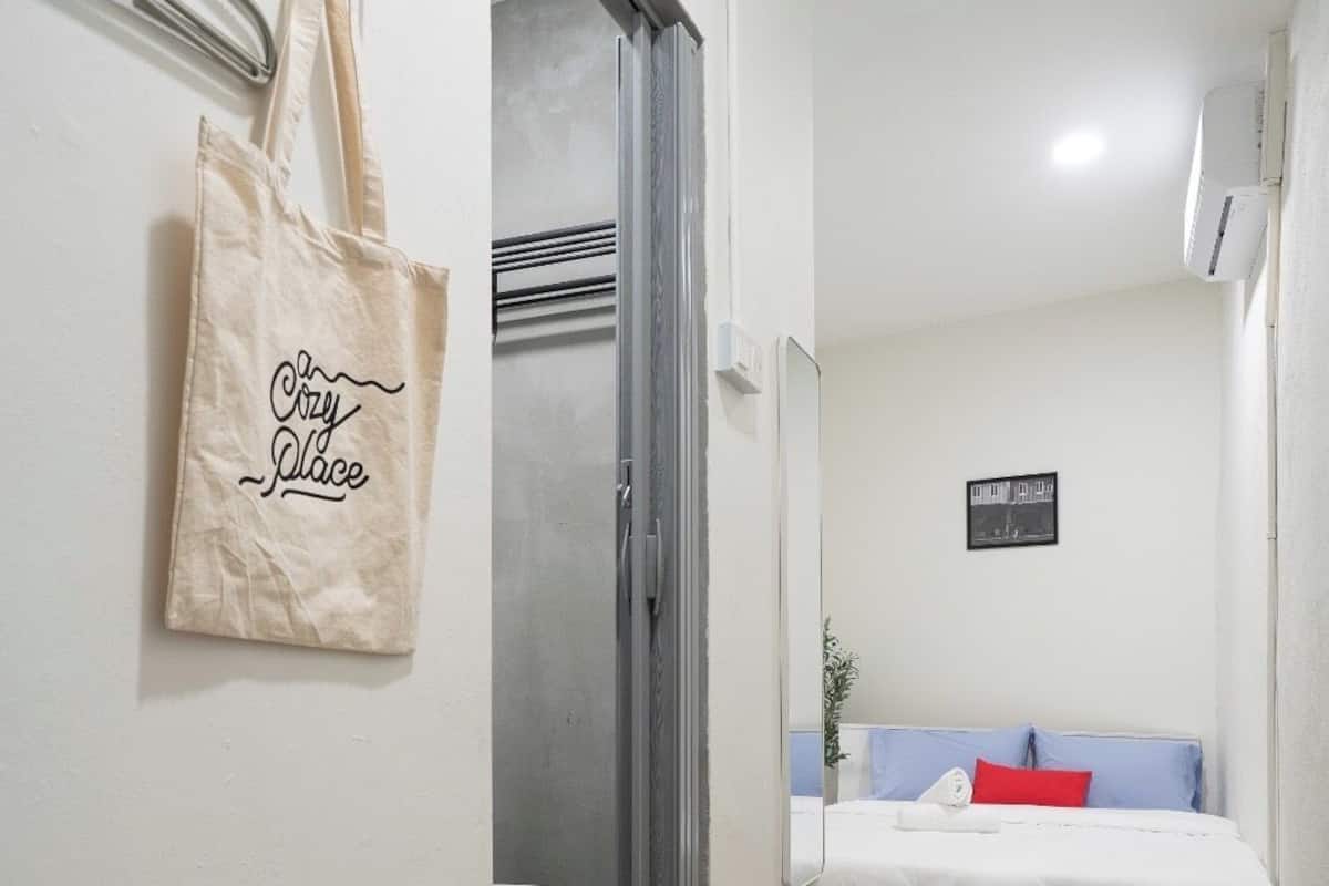 A small, compact room with a bed, a toilet, and a shower. There are two bags hanging on the wall, one with a 'Crazy Place' text and another with 'Washday' text.