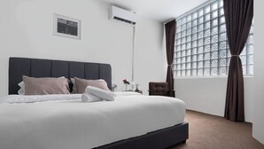 A neatly made bed with white linens and a dark headboard, a small bedside table with a vase, and a window with curtains. - A Cozy Place Penang (George Town)