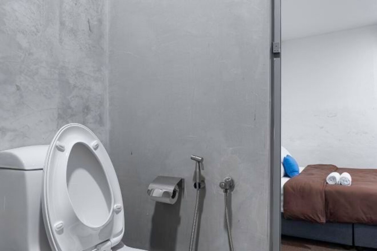 A bathroom with a toilet, a shower, and a bed with a brown blanket and two rolled towels.