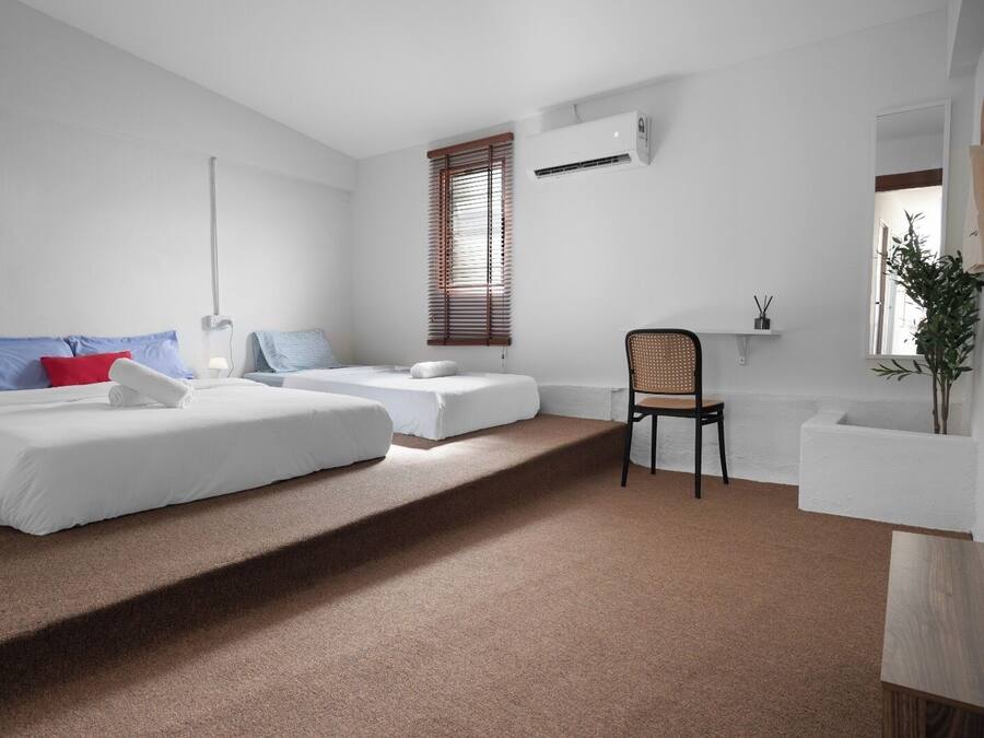 Una habitación de hotel moderna con dos camas, una silla, una mesita y una ventana con persianas.