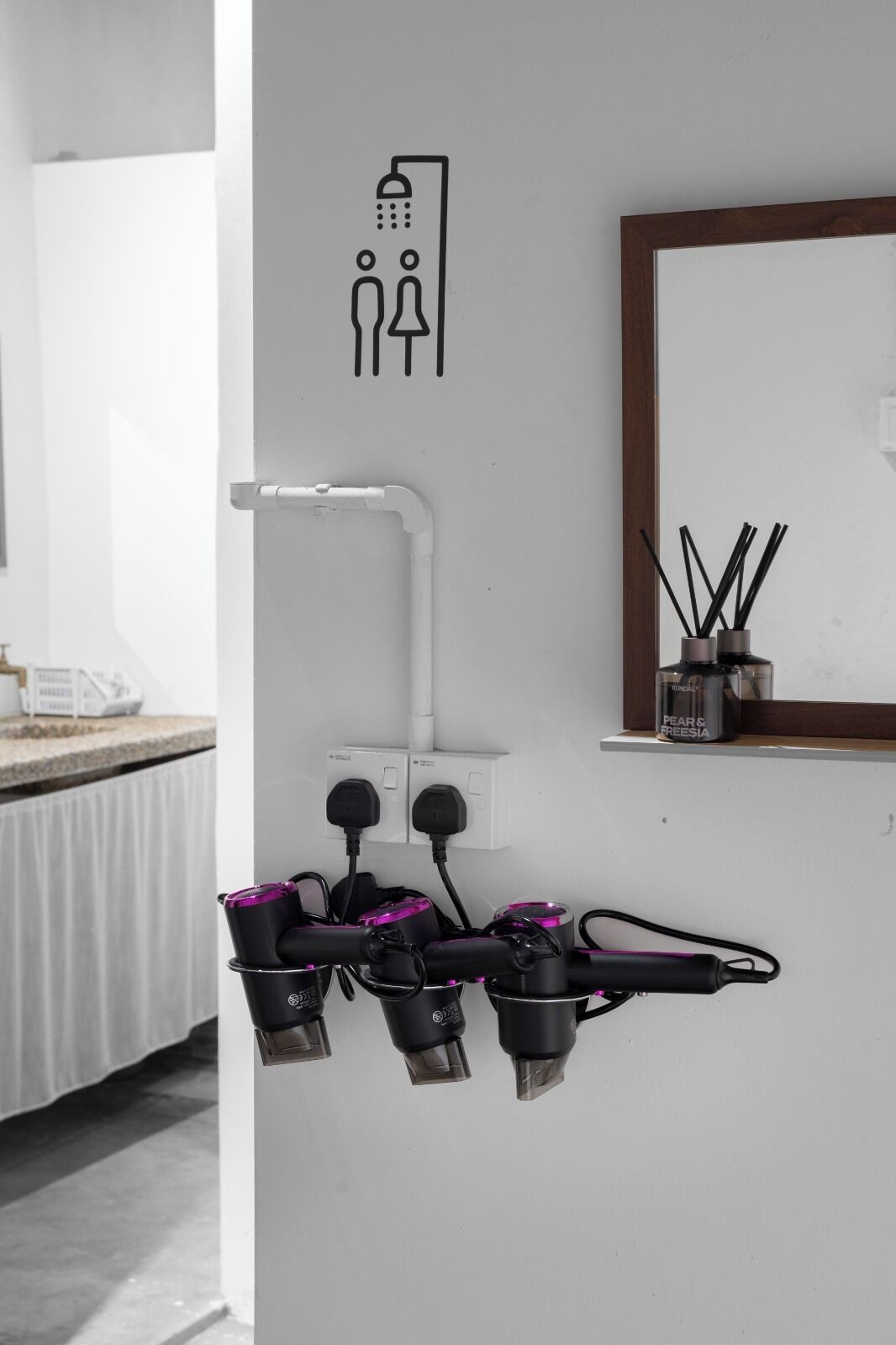 A bathroom with a shower icon, a towel rack with black and purple towels, and a shelf with a diffuser and reed diffuser.