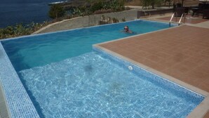 A swimming pool with a view of the ocean, surrounded by a patio area with chairs and a table. - Secluded modern villa with pebble beach near Unesco heritage city (Cidade Velha)