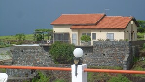 A coastal house with a stone wall and a red-tiled roof, overlooking the sea. - Secluded modern villa with pebble beach near Unesco heritage city (Cidade Velha)