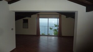 A spacious room with a large window overlooking the sea, a tiled floor, and a wooden ceiling. - Secluded modern villa with pebble beach near Unesco heritage city (Cidade Velha)