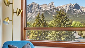 A room with a view of mountains through a window, a blue armchair with a pillow, and a floor lamp with three shades.